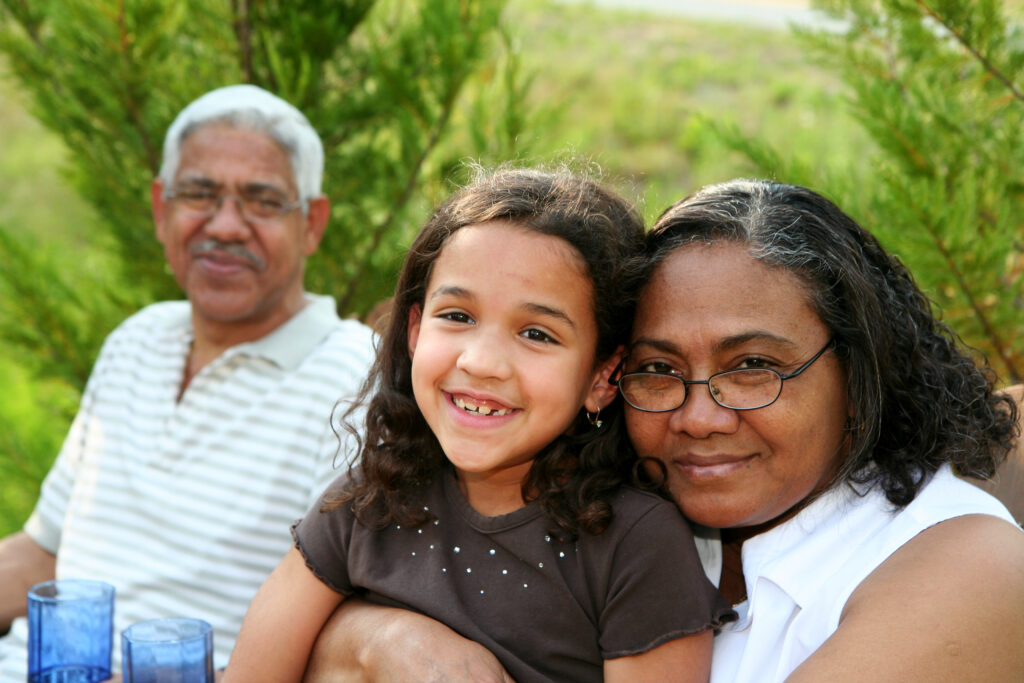 Older Hispanic woman sitting on bench with husband and granddaughter