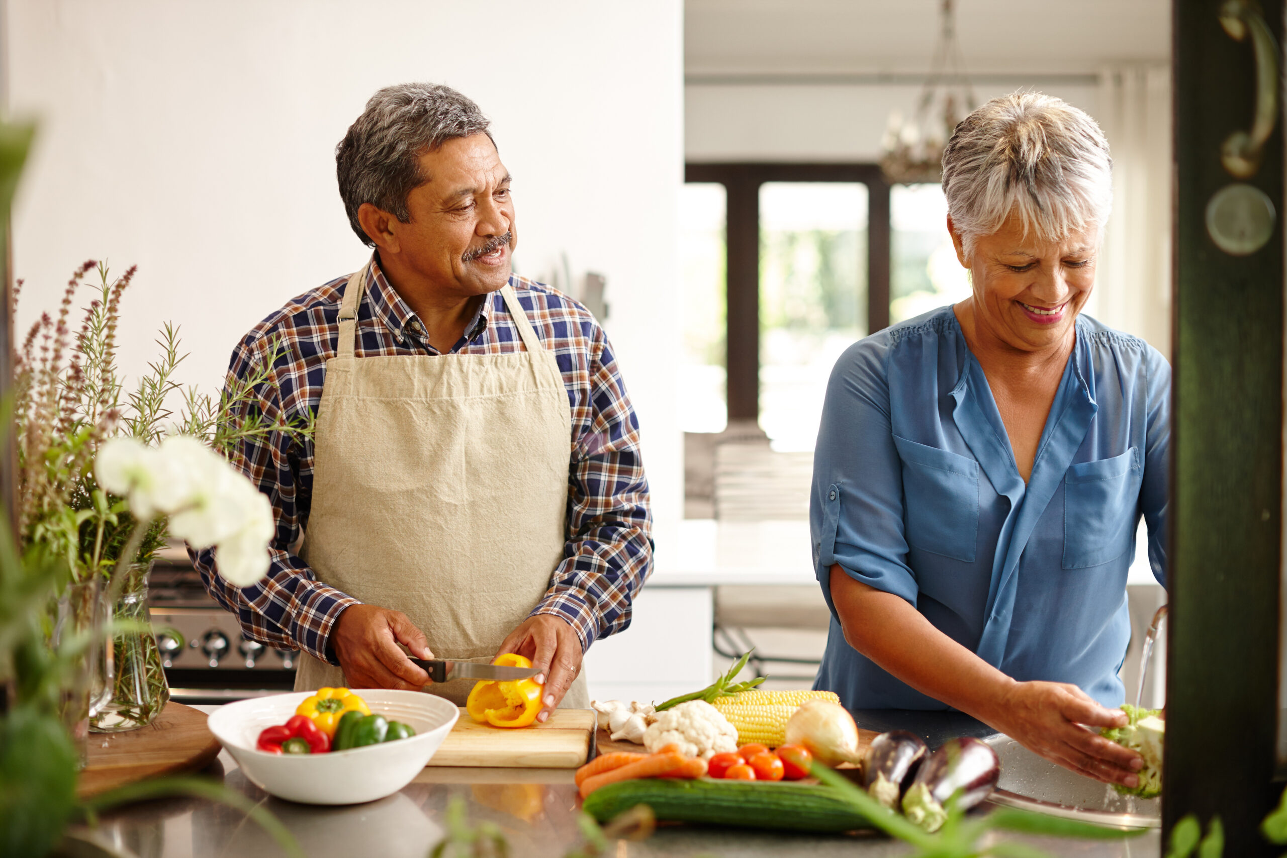 Food, elderly couple and cooking while happy in kitchen of their home. Teamwork or help, vegetables and senior married people preparing a meal for dinner or lunch together in their house