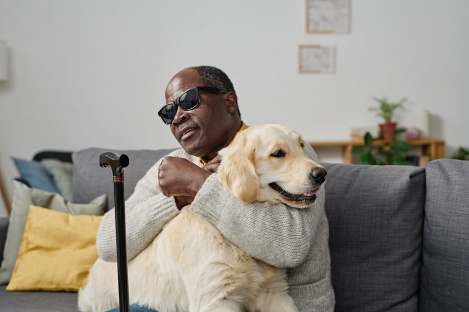 Mature Black man hugging his guide dog while sitting on sofa at home